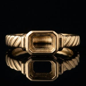 May include: A gold ring featuring an empty rectangular setting designed for a gemstone. The band displays a distinct twisted rope texture on both sides of the central mount, which has a smooth, polished finish and a hollow, open center.
