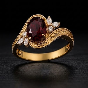 Può includere: Un anello in oro con una grande pietra preziosa rosso scuro dal taglio ovale come elemento centrale. La fascia e la montatura presentano intricate incisioni a forma di foglia, arricchite da diverse piccole pietre bianche rotonde e marquise.