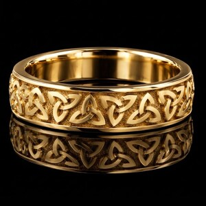 May include: A polished gold band ring featuring a continuous embossed pattern of repeating triquetra knots around the entire exterior surface. The metal has a reflective finish with recessed areas that highlight the intricate Celtic knotwork design.