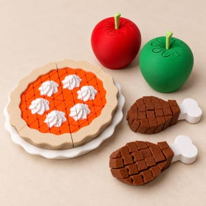 May include: A toy set featuring a round orange pie with white whipped cream dollops on a white plate, a red apple, a green apple, and two brown toy chicken drumsticks with white bone ends, all arranged together on a neutral surface.