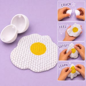 May include: A white plastic egg shell that opens to reveal a flexible, textured fried egg toy. The egg features a white outer area and a yellow centre, both covered in a small hexagonal pattern. The toy is shown being cracked, felt, and folded.