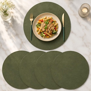 Op de afbeelding: Een set van vier ronde, donker olijfgroene placemats met een getextureerd oppervlak. Op één placemat staat een wit keramieken bord gevuld met penne pasta, broccoli en tomaten, vergezeld door een goudkleurige vork en een goudkleurig mes.