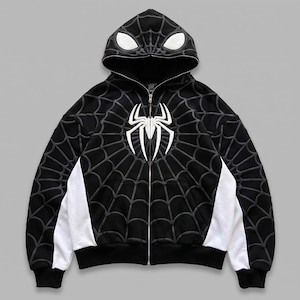 May include: A black zip-up hoodie featuring a white spider emblem on the chest and a spiderweb pattern across the body and sleeves. The hood includes two white eye-shaped patches, and the garment has white side panels and a full-length zipper.