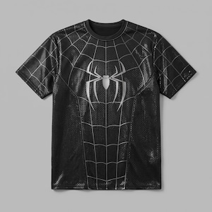 May include: A black short-sleeved t-shirt featuring a silver spider emblem on the chest and a silver spiderweb pattern extending across the front. The fabric has a subtle, repeating textured grid design throughout the entire garment.