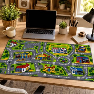 May include: A rectangular play mat featuring a colorful printed city map with roads, a hospital, a police station, a fire station, and various buildings on a green background. The mat has a gray border and depicts a network of streets for toy cars.