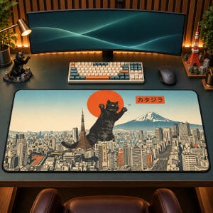 Pode incluir: Um tapete de secretária retangular com uma ilustração gráfica de um gato preto gigante sobre uma paisagem urbana com a Torre de Tóquio e o Monte Fuji ao fundo. O design inclui um grande sol laranja e o texto japonês "カタジラ" numa caixa vermelha.