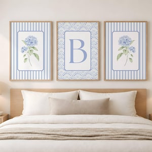 May include: A set of three framed wall art prints. The two outer prints feature blue hydrangea illustrations on a white background with blue vertical stripes. The center print displays a large blue letter B on a patterned background.