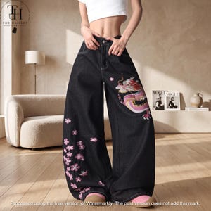 Puede incluir: Pantalones vaqueros negros de tiro alto con pernera ancha. La pierna izquierda muestra un dragón bordado en rosa y blanco, mientras que la pierna derecha está decorada con un grupo de flores de cerezo bordadas en rosa y costuras blancas.
