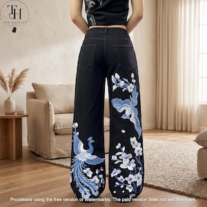 Könnte beinhalten: Schwarze Jeans mit weitem Bein und aufwendiger blau-weißer Stickerei eines Pfaus auf dem linken Bein sowie eines Vogels mit Kirschblütenzweigen auf dem rechten Bein. Die Jeans hat eine hohe Taille, Gürtelschlaufen und zwei Gesäßtaschen.