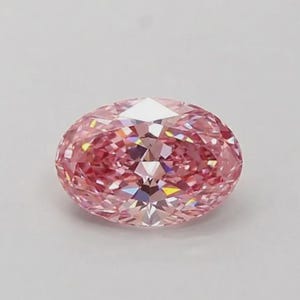 May include: An oval-cut gemstone with a vibrant pink hue and numerous facets that create a brilliant, reflective surface. The stone displays a symmetrical shape with sharp, geometric edges throughout its structure, catching light to produce sparkles.