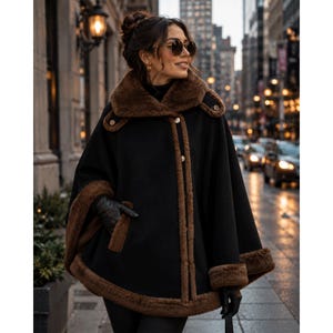 May include: A black cape featuring a wide brown faux fur collar, brown faux fur trim along the front opening, and brown faux fur cuffs. The garment includes a series of buttons down the front and is worn with black gloves and dark sunglasses.