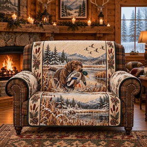 May include: A quilted loveseat cover featuring a scenic landscape with a brown retriever dog carrying a mallard duck in its mouth. The design includes snowy mountains, pine trees, cattails, and pinecones, with plaid fabric on the armrests.