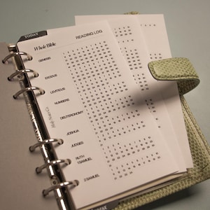 May include: A light green textured binder with a silver six-ring metal mechanism holding white paper inserts. The visible page features a Whole Bible reading log with numbered columns for books including Genesis, Exodus, Leviticus, and Numbers.