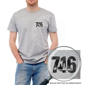 May include: A light gray t-shirt with the number "716" printed in black on the chest. The "716" design incorporates a cityscape silhouette. The shirt is short-sleeved and made of a soft material.