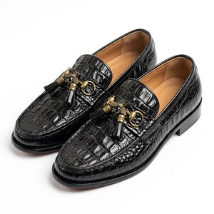 Puede incluir: Un par de mocasines negros con una textura brillante de relieve de cocodrilo. Cada zapato presenta un adorno de abeja de metal dorado con una piedra negra en el centro, acompañado de una pequeña borla negra y un detalle de bocado dorado.