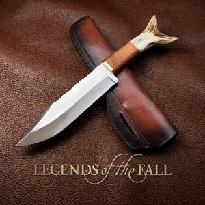 Puede incluir: Un cuchillo de hoja fija con hoja de acero plateado, mango envuelto en cuero marrón y pomo de asta de color claro. El cuchillo descansa sobre una funda de cuero marrón a juego. El texto "LEGENDS of the FALL" aparece bajo el cuchillo.