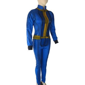 Op de afbeelding: Een blauwe jumpsuit met een hoge kraag, lange mouwen met zwarte boorden en een centraal verticaal goudkleurig paneel. Het kledingstuk is voorzien van een gouden tailleband en gestructureerde blauwe stoffen panelen langs de zijkanten van de romp en benen.
