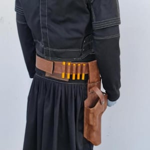 May include: A black jacket with white stitching and a high collar, paired with a black pleated skirt. A brown leather belt features a row of five yellow-tipped cartridges and a matching brown leather holster attached to the side of the belt.
