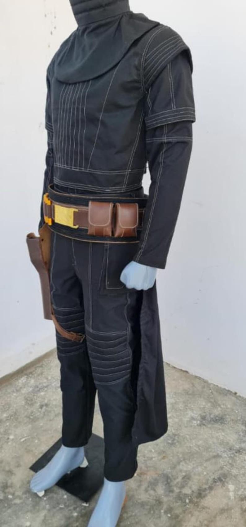 May include: A black long-sleeved tunic and matching trousers featuring white topstitching, a high collar, and a dark brown utility belt with two pouches and a gold buckle. A brown holster is attached to the belt, and the outfit includes a long back panel.
