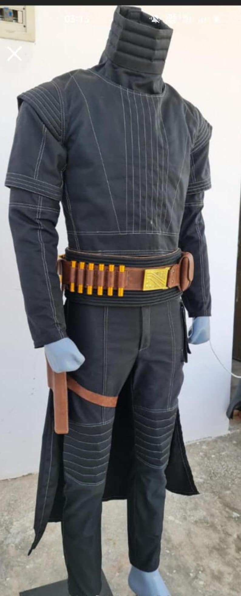 May include: A black long-sleeved jacket and matching trousers with white contrast stitching, a high collar, and ribbed shoulder and knee panels. A brown leather belt features a gold rectangular buckle and yellow cylindrical inserts.
