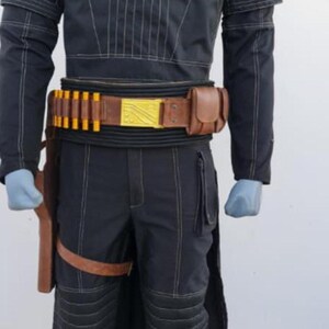 May include: A black long-sleeved shirt and matching pants with white topstitching, featuring a high neck collar, padded knee sections, and a brown leather utility belt with yellow cylindrical accents, a gold rectangular buckle, and a side holster.