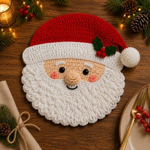May include: A round crochet Santa Claus face coaster featuring a red hat with a white pom-pom, a white beard, a beige face, black eyes, and a small sprig of green holly leaves with three red berries attached to the side of the hat brim.