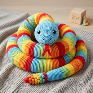 May include: A coiled crochet snake toy featuring a bright blue head with black eyes and a red forked tongue. The body is crafted with horizontal stripes in red, orange, yellow, green, and blue. The tail ends in a textured, multi-coloured rattle.