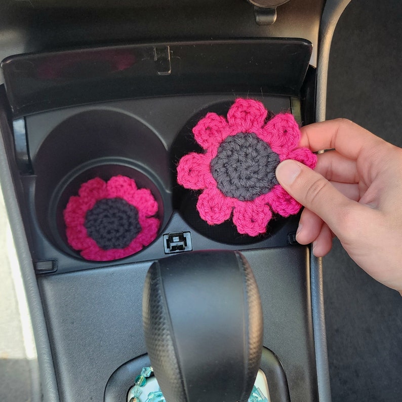 Hand placing a set of magenta pink sunflower coasters into a cars cup holders.