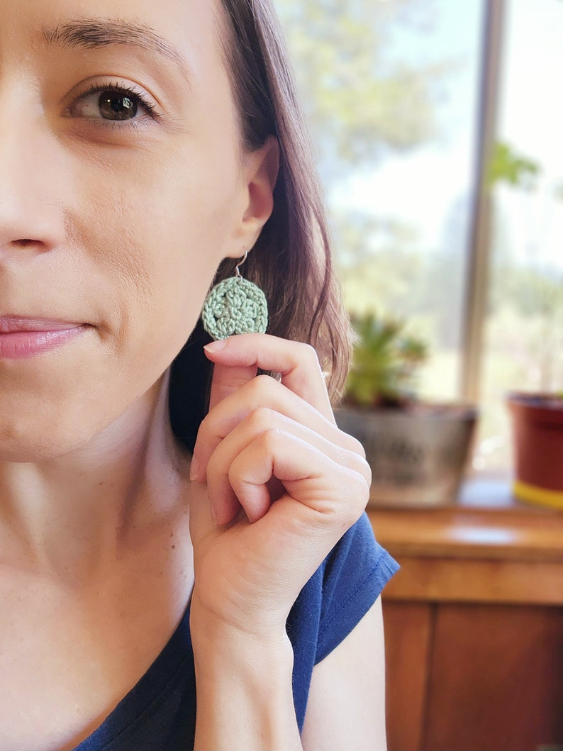 A green flower earring is modeled on a woman holding it out for size reference.