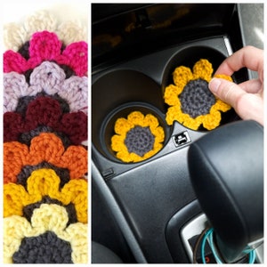 Hand places a set of crochet sunflower coasters into a cars cup holders. Crochet sunflowers shown lined up in various colors including light yellow, mustard yellow, orange, burgundy, purple, pink and cream.