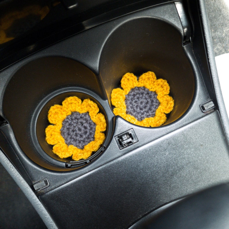 A set of mustard yellow sunflower coasters inserted in a cars cup holders.