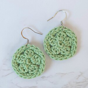 Set of 2 green crochet flower earrings on a white surface.