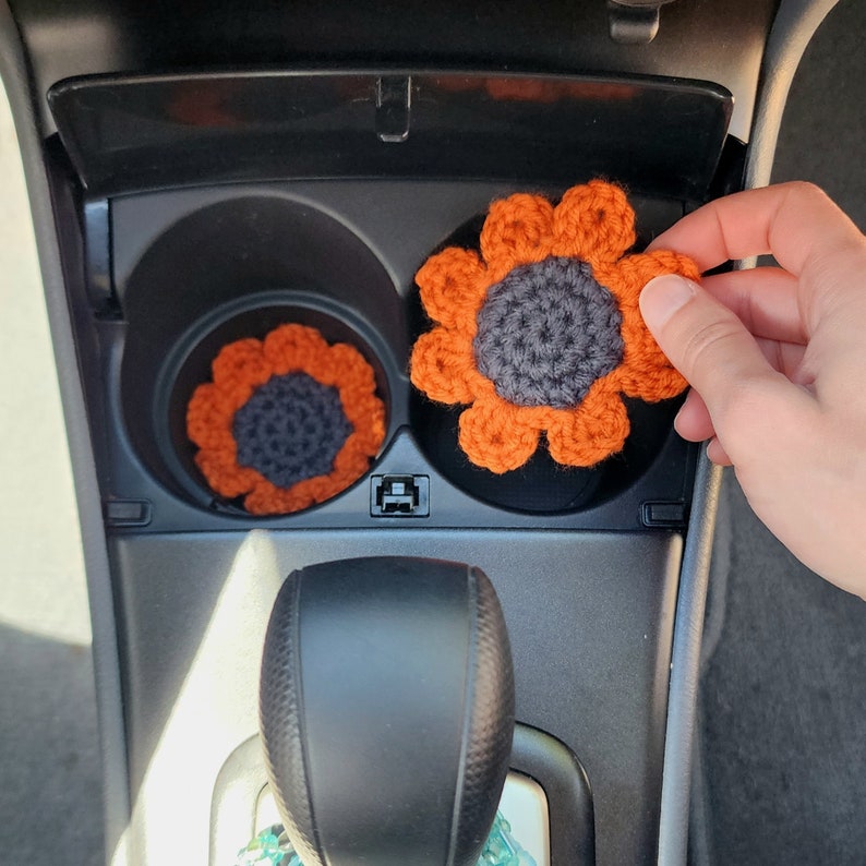 Hand placing a set of orange sunflower coasters into a cars cup holders.