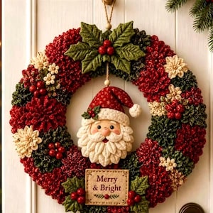 May include: A circular holiday wreath featuring red and green fabric petals, cream-colored flower accents, and red berries. A fabric Santa Claus ornament hangs in the center, and a rectangular sign below reads Merry & Bright.