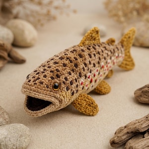 Peut inclure: Un poisson au crochet avec un corps beige et marron, des taches marron foncé et de petites touches rouges sur le côté. Le poisson présente une bouche grande ouverte, des yeux ambrés foncés et des nageoires texturées jaune moutarde.
