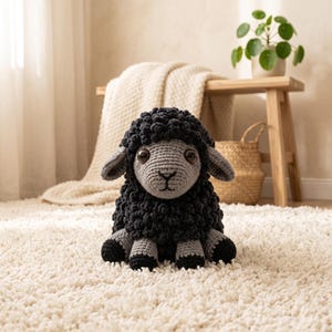 May include: A crochet sheep stuffed animal featuring a dark charcoal black textured wool body and a light gray face. The sheep has large brown plastic eyes, a stitched black nose and mouth, and matching gray and black limbs in a seated position.