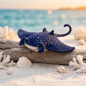 Può includere: Un peluche a forma di razza realizzato all'uncinetto in blu scuro con macchie bianche sul dorso, grandi occhi blu e neri e una lunga coda arricciata. La razza presenta una parte inferiore color crema chiaro ed è lavorata a maglia.