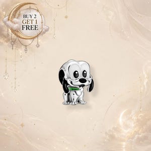 Puede incluir: Un charm de plata con forma de perro de dibujos animados con grandes ojos negros, nariz negra y un collar verde. El charm tiene la palabra Pandora grabada en el lateral. Un gráfico circular en la esquina superior izquierda muestra el texto BUY 2 GET 1 FREE.
