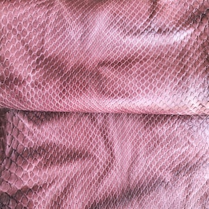 Puede incluir: Una lámina de piel de serpiente de color malva que presenta un patrón de escamas distintivo y repetitivo en toda la superficie. El material muestra un brillo sutil con variaciones de tono, desde el morado rosado claro hasta sombras más profundas.