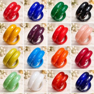 May include: A collection of sixteen pairs of faceted bangle bracelets in various solid colours including red, blue, green, black, yellow, purple, orange, pink, lime, and white. Each bangle features a geometric, multi-faceted surface texture.