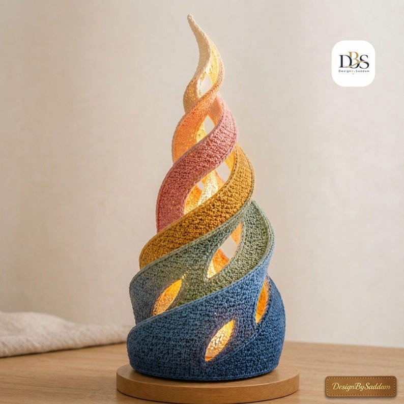 May include: A spiral-shaped table lamp featuring a textured, crocheted exterior with a gradient color scheme transitioning from dark blue at the base to light yellow at the top. The lamp emits a warm internal glow through its open, twisted design.