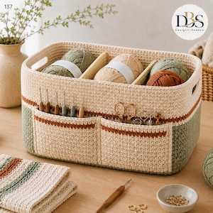 Puede incluir: Una cesta de almacenamiento rectangular de ganchillo en color crema, verde salvia y terracota. La cesta cuenta con dos bolsillos frontales con ganchillos y tijeras, y divisores internos con ovillos de lana en verde, beige y marrón.