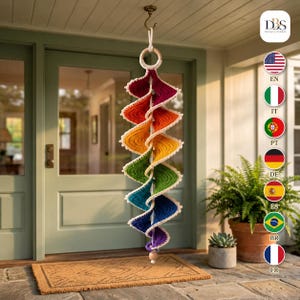 May include: A hanging spiral decoration featuring a vibrant rainbow gradient of crocheted yarn in red, orange, yellow, green, blue, and purple. The structure is suspended from a wooden ring and features a white crocheted border along the edges.