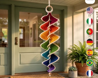 Puede incluir: Una decoración en espiral colgante que presenta un vibrante degradado de arcoíris de hilo de ganchillo en rojo, naranja, amarillo, verde, azul y morado. La estructura está suspendida de un anillo de madera y tiene un borde de ganchillo blanco.