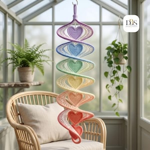 May include: A hanging spiral decoration featuring a series of crocheted hearts in a gradient of colors including purple, blue, green, yellow, orange, and red. The structure is suspended from a single loop at the top, creating a vertical display.