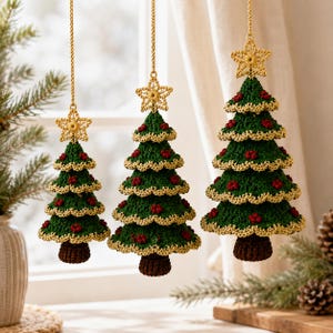 Puede incluir: Tres adornos colgantes para árbol de Navidad hechos de hilo de ganchillo verde con bordes dorados y pequeños detalles de bayas rojas. Cada árbol está rematado con una estrella de ganchillo dorada y colgado de un cordón dorado.