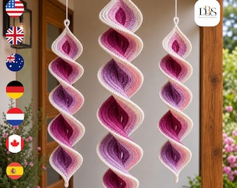 May include: Three hanging spiral ornaments crafted from crochet yarn in an ombre gradient of cream, light pink, magenta, and deep purple. Each piece features a twisted, elongated shape suspended by a white string, with the text DBS Design-System.