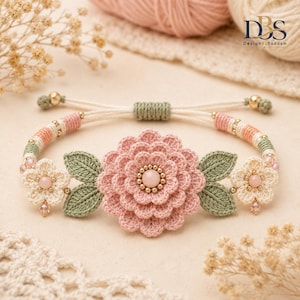 May include: A handmade crochet bracelet featuring a large central pink flower with a round bead center, flanked by two green crocheted leaves and two smaller cream-colored flowers. The band consists of cream, pink, and green woven cord.