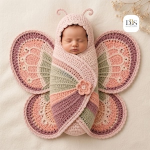 May include: A crochet baby swaddle featuring a hood with antennae and large butterfly wings in shades of dusty pink, sage green, and mauve. The swaddle is secured with a small crocheted flower accent. The logo DBS Design-Season is visible.