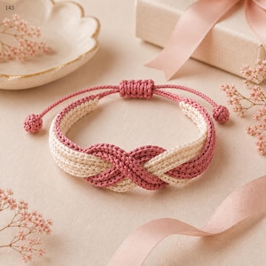 Könnte beinhalten: Ein geflochtenes Kordelarmband mit einem Unendlichkeitsknoten-Design in abwechselnden Farben in Altrosa und Creme. Das Armband verfügt über einen verstellbaren Schiebeknotenverschluss mit zwei kleinen kugelförmigen Enden und einer strukturierten Flechtoptik.